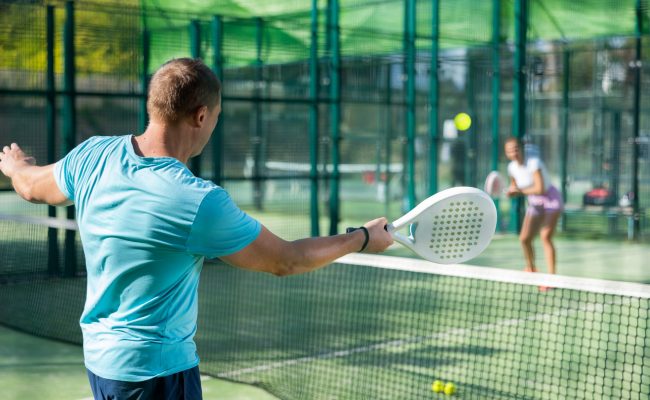 Rear view of man in sportswear playing padel tennis on court. Racket sport training outdoors.